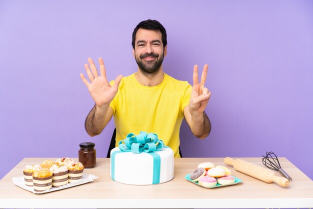 Uomo in un tavolo con una grande torta contando sette con le dita