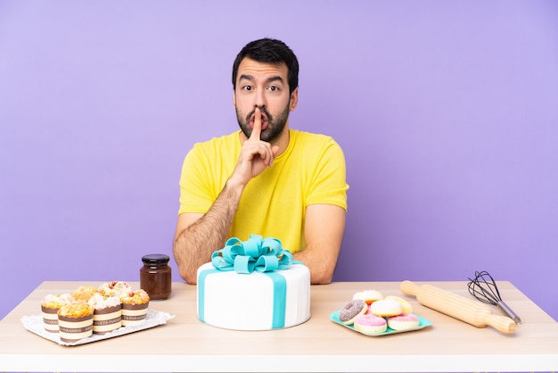 Uomo in una tabella con una grande torta che mostra un segno di silenzio gesto mettendo il dito in bocca