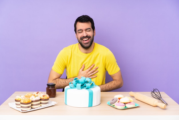 Uomo in una tabella con una grande torta che sorride molto