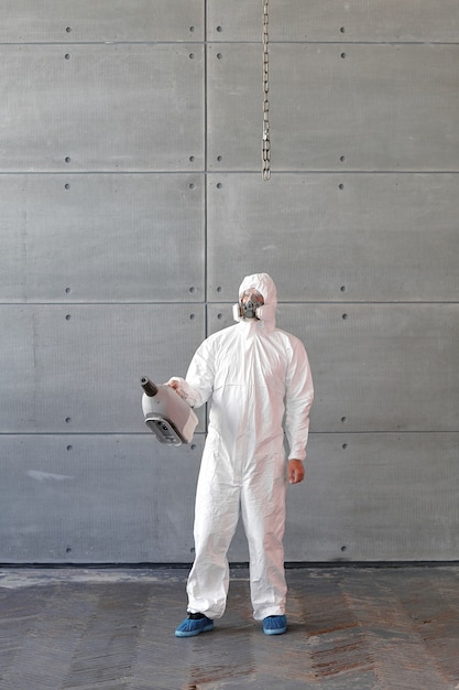 Uomo in una tuta di protezione chimica e una maschera antigas. Il ragazzo tiene in mano una pistola a spruzzo. Decontaminazione in speciale