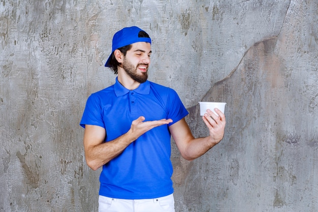 Uomo in uniforme blu che tiene un bicchiere di plastica da asporto.