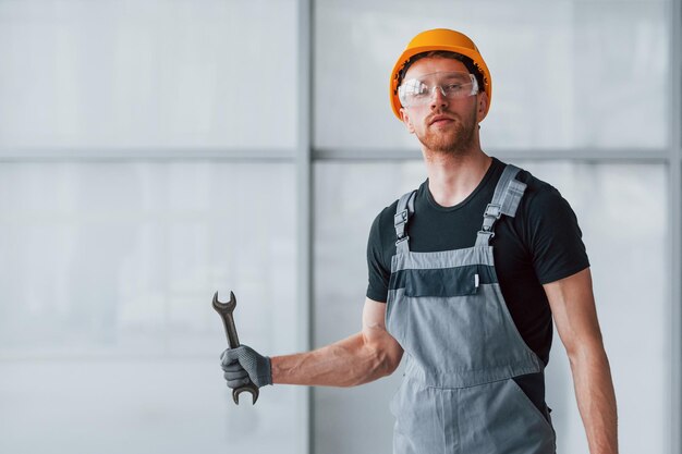 Uomo in uniforme grigia con chiave in mano in piedi all'interno in un grande ufficio moderno durante il giorno