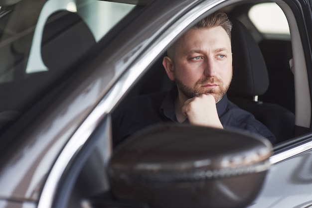 Uomo in vestiti ufficiali che prova la sua nuova automobile nel salone dell'automobile