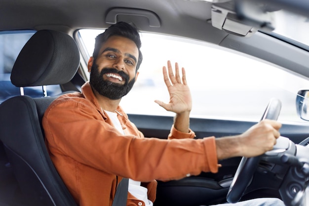 Uomo indiano allegro che fa un gesto di saluto dal sedile del conducente in auto