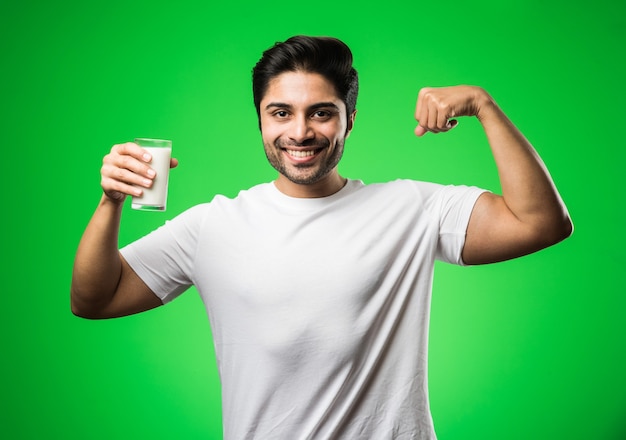 Uomo indiano che beve latte in un bicchiere mentre sta in piedi isolato