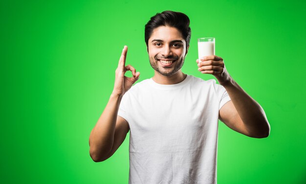 Uomo indiano che beve latte in un bicchiere mentre sta in piedi isolato