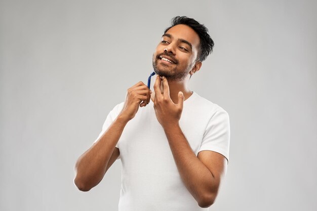 uomo indiano che si rascia la barba con una lama da rasoio