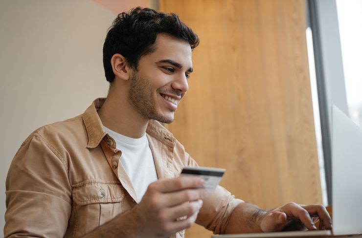 Foto uomo indiano che utilizza computer portatile che tiene la carta di credito acquisti in linea