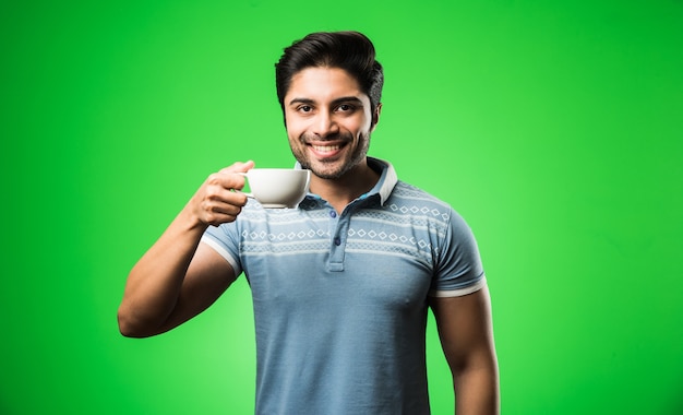 Uomo indiano con una tazza o una tazza di tè o caffè. Bere, presentare o tenere in mano stando in piedi isolato