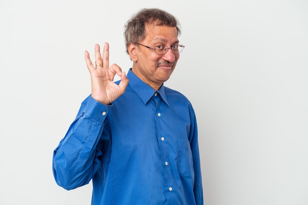 Uomo indiano di mezza età isolato su sfondo bianco strizza l'occhio e tiene un gesto ok con la mano.