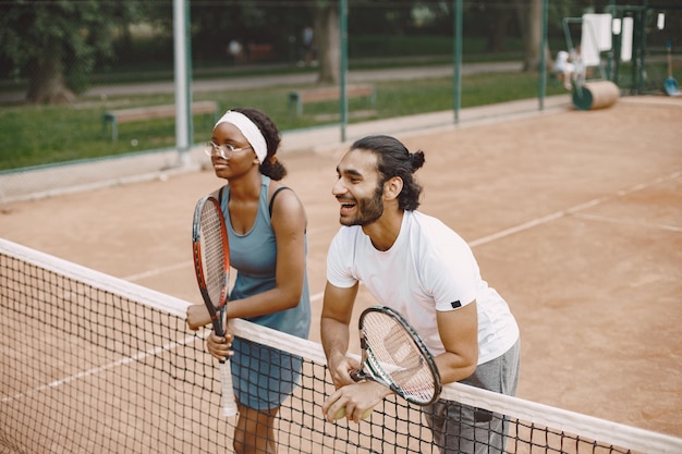 Uomo indiano e donna nera americana in piedi su un campo da tennis