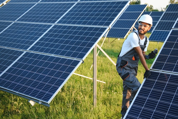 Uomo indiano in uniforme che lavora vicino al pannello solare