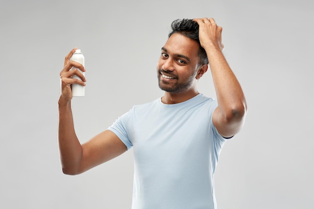 uomo indiano sorridente che applica spray per capelli su grigio