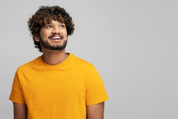 Uomo indiano sorridente con capelli ricci alla moda che indossa una maglietta gialla, guardando lontano, copia spazio