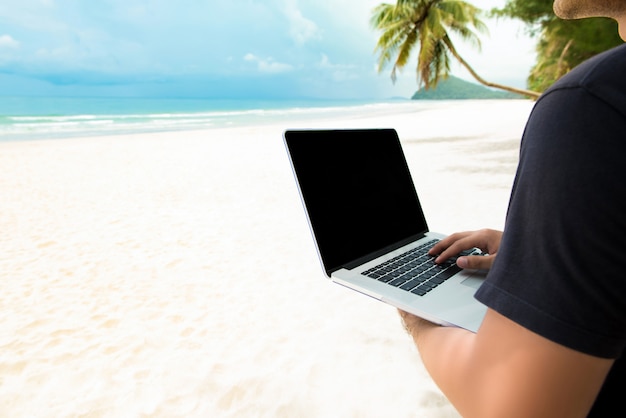 Uomo indipendente che lavora con il computer portatile in linea alla spiaggia