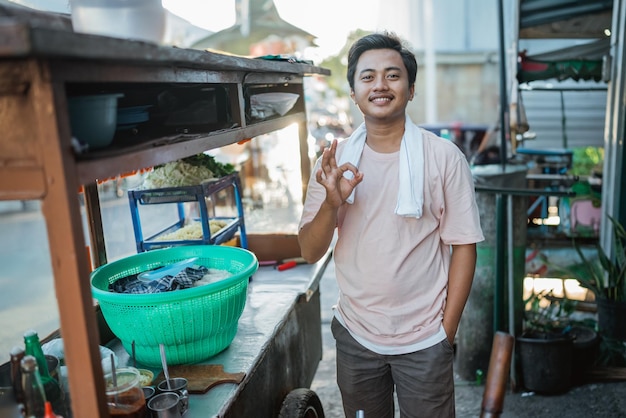 Uomo indonesiano in piedi dietro il carrello del cibo con un gustoso gesto della mano