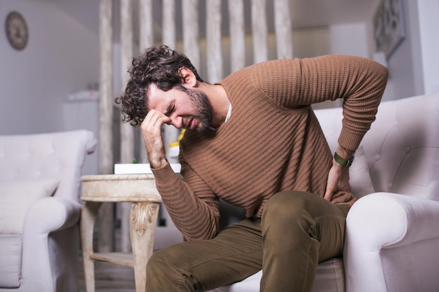 Uomo infelice che soffre di mal di schiena a casa. Mal di schiena lombare . L'uomo avverte mal di schiena massaggiando i muscoli doloranti, l'uomo triste soffre di lombalgia