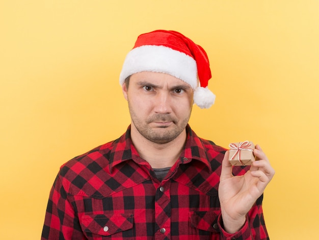 Uomo infelice e turbato con un cappello rosso tiene in mano un piccolo dono con disgusto