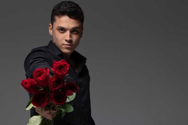 uomo innamorato che indossa abiti scuri con in mano un mazzo di rose rosse foto in studio sfondo grigio