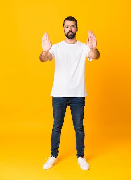 Uomo integrale con la barba sopra la parete gialla isolata che fa gesto di arresto e deludente