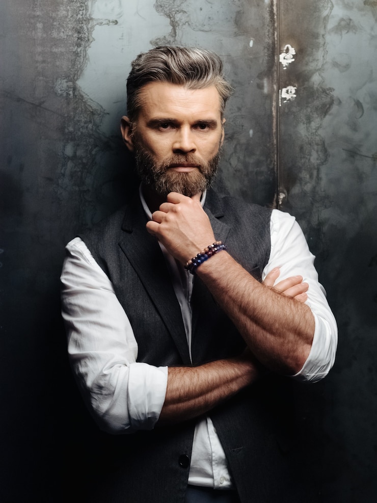 Foto uomo invecchiato premuroso che indossa camicia bianca, gilet grigio e pantaloni isolati su sfondo scuro.