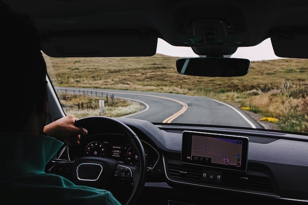 Uomo irriconoscibile che guida un'auto su una strada di campagna vuota vista dall'interno dell'auto