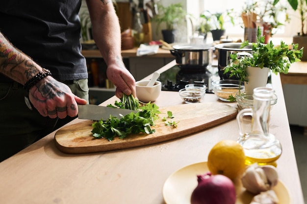 Uomo irriconoscibile che taglia il prezzemolo in cucina