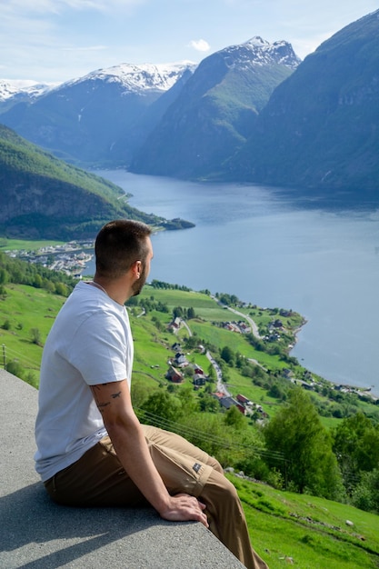 Uomo irriconoscibile seduto sul bordo di un punto di vedetta con il fiordo sullo sfondo in Norvegia