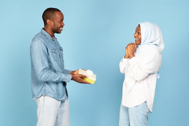 Uomo islamico nero che dà confezione regalo alla moglie su sfondo blu