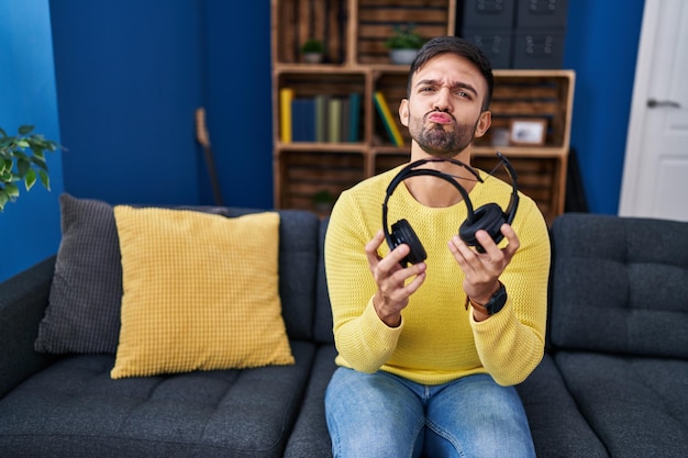 Uomo ispanico che tiene le cuffie rotte guardando la telecamera che soffia un bacio essendo adorabile e sexy. espressione d'amore.