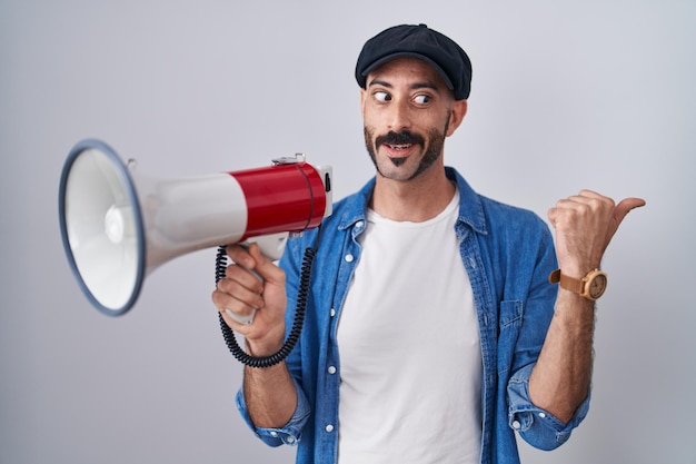 Uomo ispanico con la barba che grida attraverso il megafono che punta il pollice verso l'alto sorridendo felice con la bocca aperta