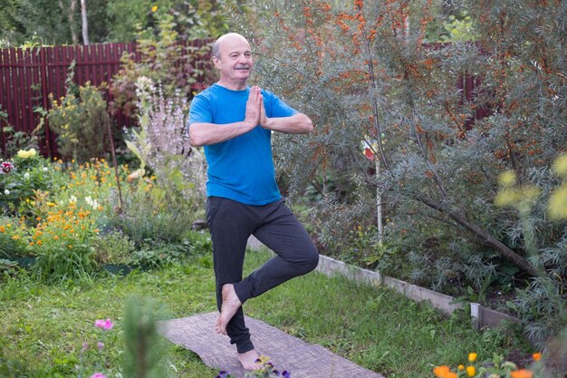 Uomo ispanico senior che sta nella posa di yoga dell'albero in giardino