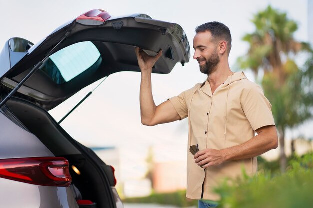 Uomo ispanico sorridente che compra automobile nuova Autista barbuto di successo che apre il bagagliaio dell'auto per pianificare un viaggio su strada