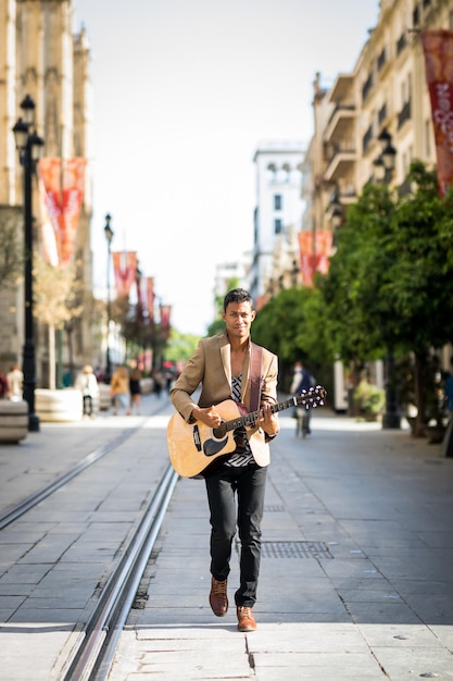 Uomo latino che cammina mentre suona la chitarra su una strada trafficata (verticale)