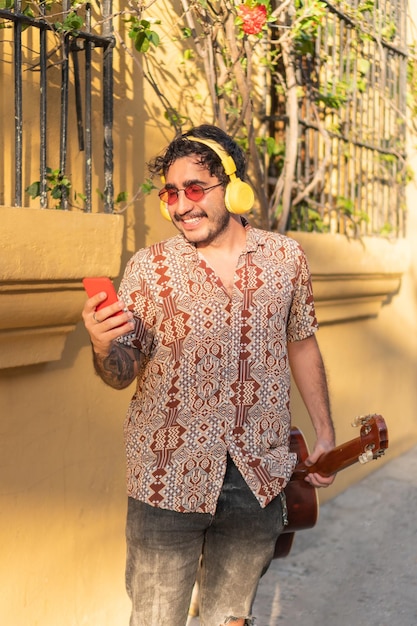 Uomo latino che cammina portando la chitarra e controllando il suo telefono cellulare