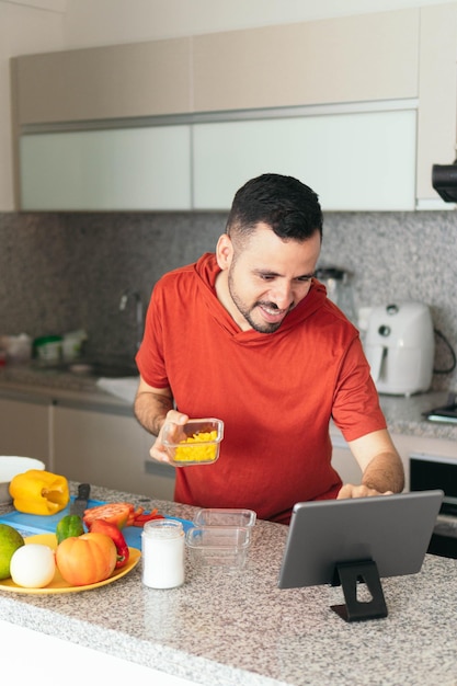 Uomo latino che cucina e usa il suo tablet in cucina