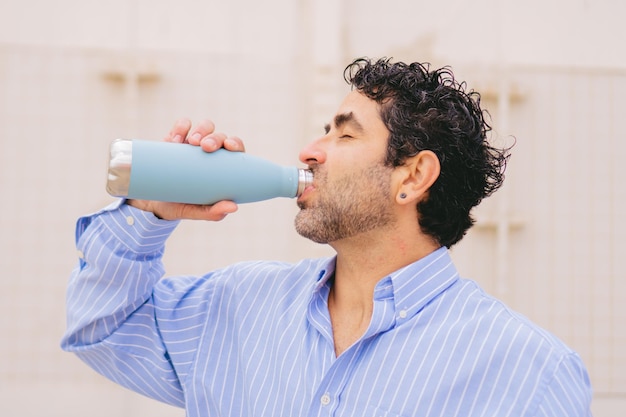Uomo latino di mezza età in camicia che beve acqua da una bottiglia riutilizzabile