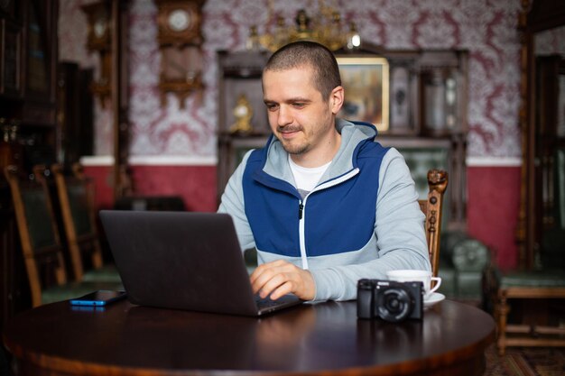 Uomo libero professionista con laptop e fotocamera che lavora e guarda nel laptop in interni vintage