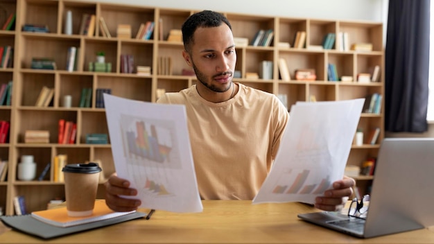 Uomo libero professionista maschio arabo che lavora con documenti e laptop in ufficio a casa che controlla il panorama dei documenti finanziari