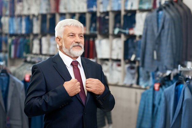 Uomo maggiore che sceglie vestiti eleganti in negozio per gli uomini.