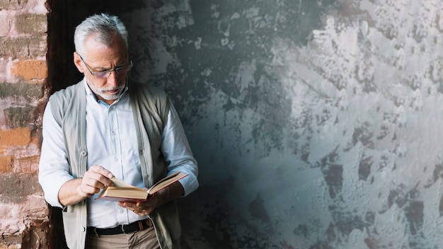 Uomo maggiore che si appoggia al libro di lettura del muro di mattoni