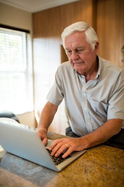 Uomo maggiore che utilizza computer portatile in cucina a casa