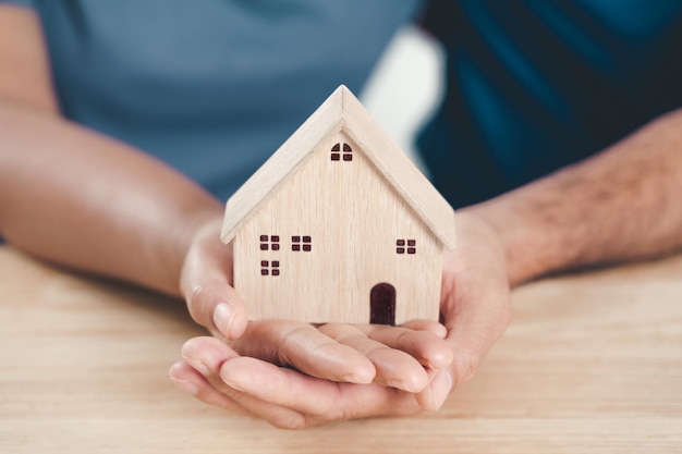 Uomo marito e donna moglie mani che tengono casa di legno sulla tavola di legno sfondo casa di famiglia