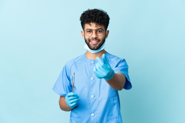 Uomo marocchino dentista che tiene strumenti isolati sul gesto di fare soldi blu