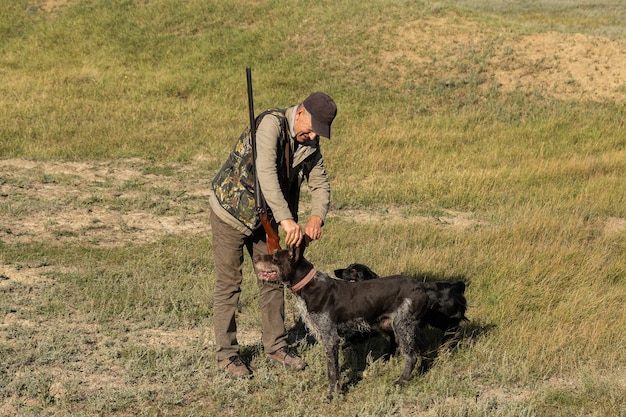 Uomo maturo cacciatore con una pistola mentre cammina sul campo con i tuoi cani