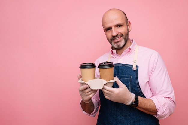 Uomo maturo calvo che mangia caffè in tazze di cartone riciclabili