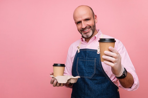 Uomo maturo calvo che mangia caffè in tazze di cartone riciclabili