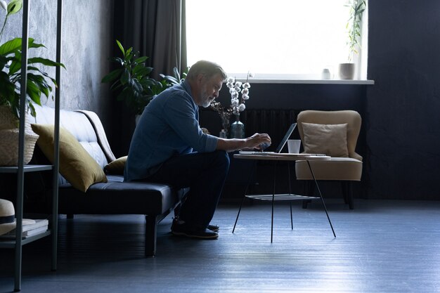 Uomo maturo che acquista online sul computer portatile, utilizzando la carta di credito a casa.