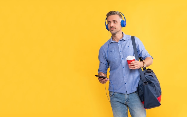 Uomo maturo che ascolta musica in auricolari in chat sul telefono tenere borsa sportiva bere caffè stile di vita