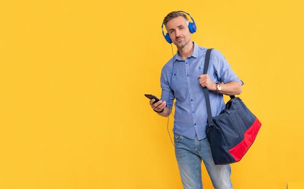 Uomo maturo che ascolta musica sul telefono tiene la borsa sportiva su sfondo giallo copia spazio messaggio